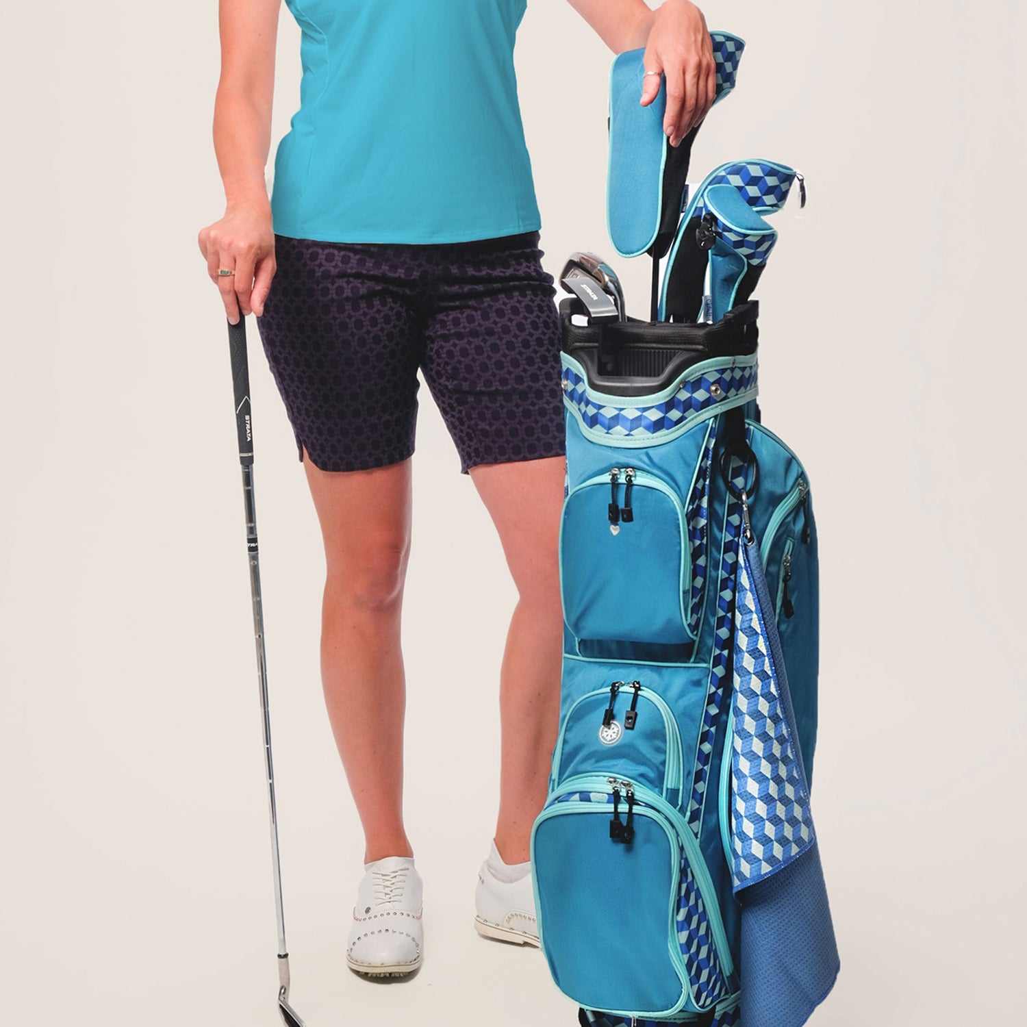 Woman in blue golf attire holding a golf club and blue golf bag on a light gray background
