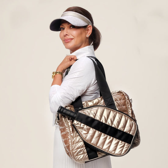 Woman holding a gold and black duffel bag against a plain background